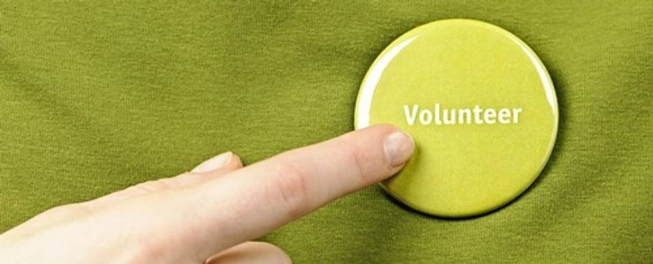 Someone pointing to a volunteer button on their shirt.