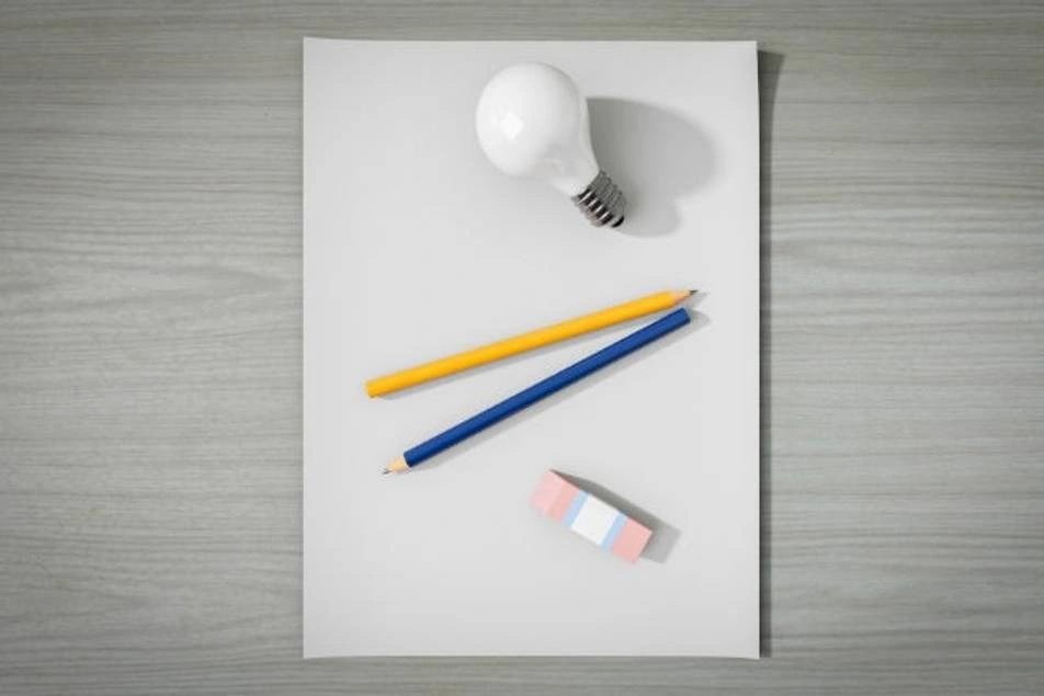 Una hoja de papel con unos lápices, una bombilla de luz y un borrador