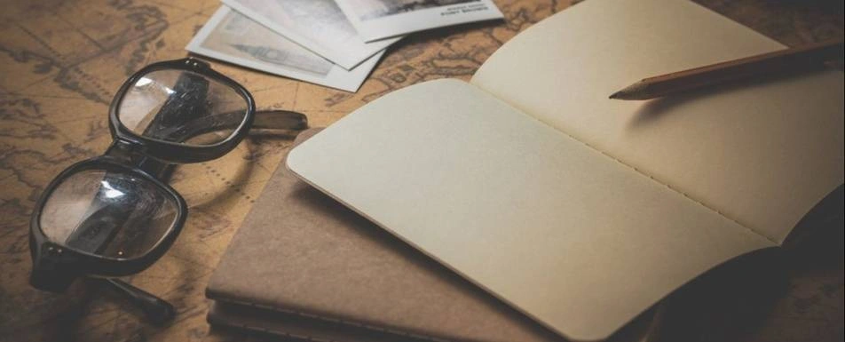 A table with a pair of glasses, book and a pencil.