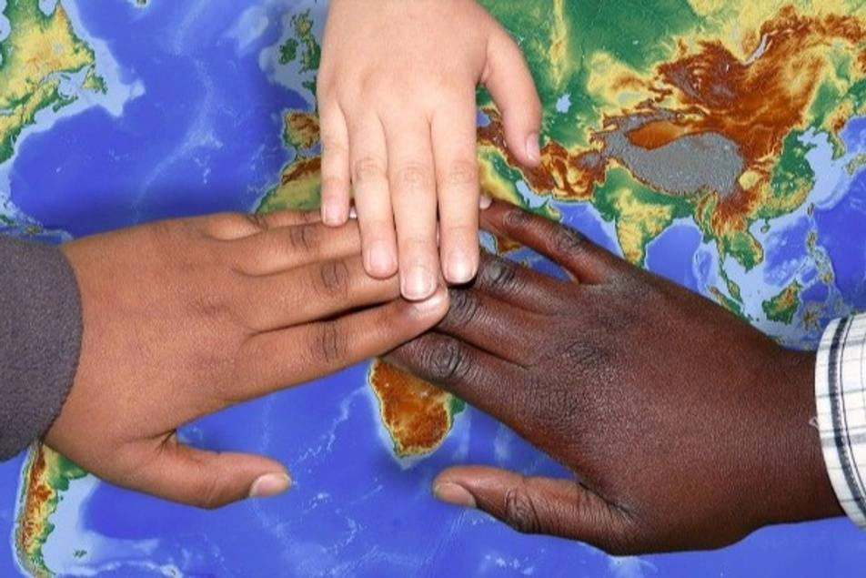 3 manos de personas de diferente origen étnico unidas sobre un mapa del mundo