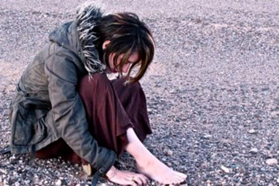Una mujer con pies descalzos sentada en el suelo mirando las piedras