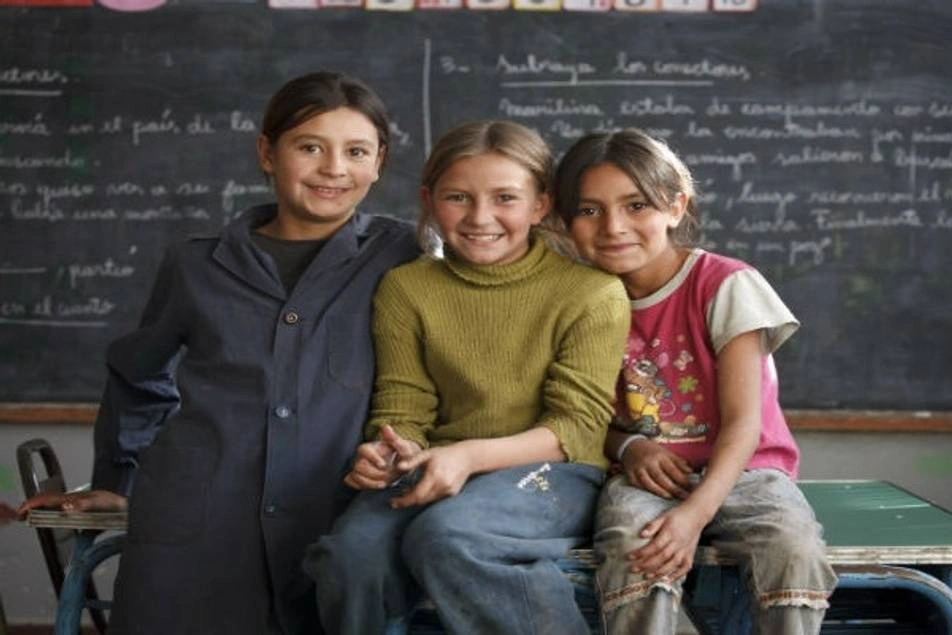 Tres niñas sonriendo a la cámara, en un aula de clases