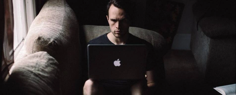 A man sitting on a couch and looking at his laptop.