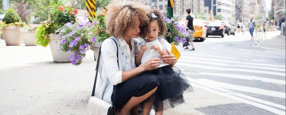 A Black woman with her daughter at an intersection.