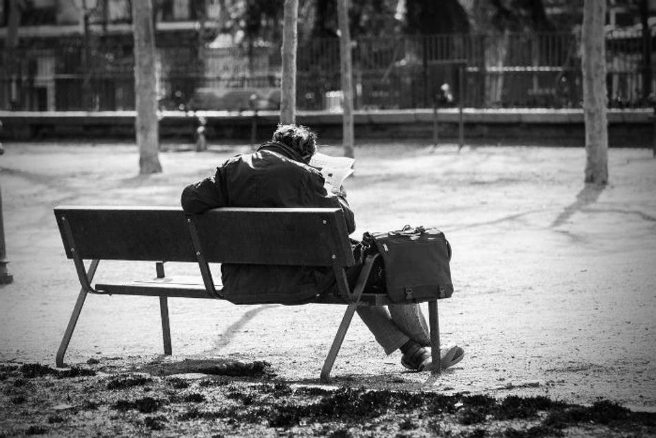 Una persona en situación de calle sentado en un banco en un parque