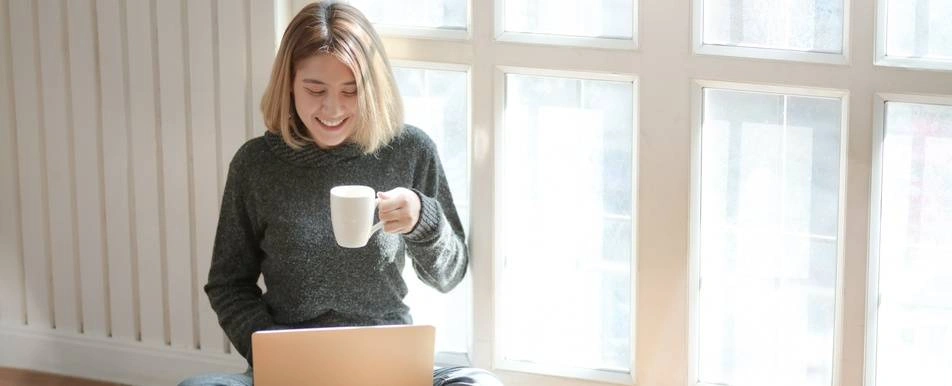woman drinking coffee smiling at laptop