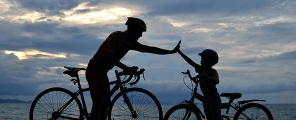 A backlit photo of a man and a little boy exchanging a high five next to their bikes.