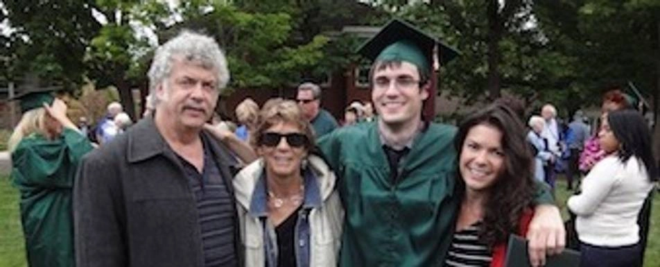 A group of people smiling. One of them is in a graduation robe and cap.