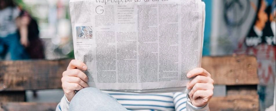 Someone with an open newspaper covering their face.