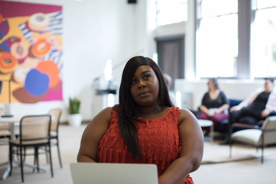 A Black woman sits thoughtfully at her laptop.