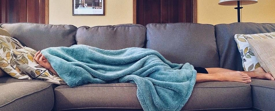 A person on a couch under a blanket.