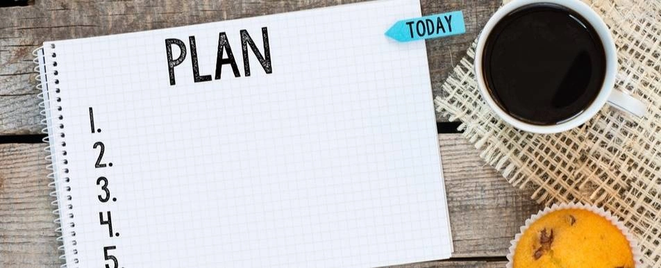 A notebook with the word 'Plan' written at the top. There is also a muffin and coffee on the table.