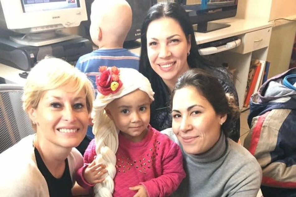 Mujeres junto a una niña con cáncer usando una peluca