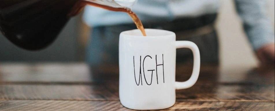 Coffee being poured into a mug that says, "Ugh."