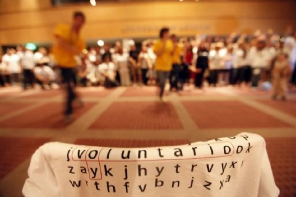 Foto de unos voluntarios participando en un evento y en primer plano una camiseta con una sopa de letras que dice voluntario