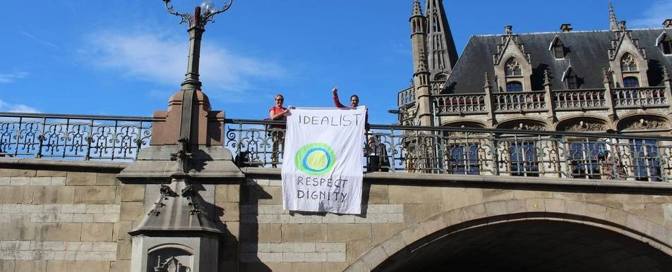 Two idealists hold a banner with the Idealist logo on it over a bridge