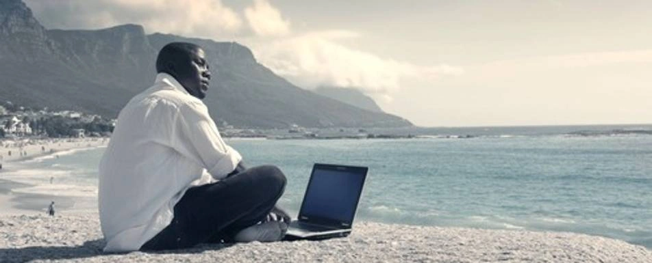 Someone sitting on a beach with their laptop.