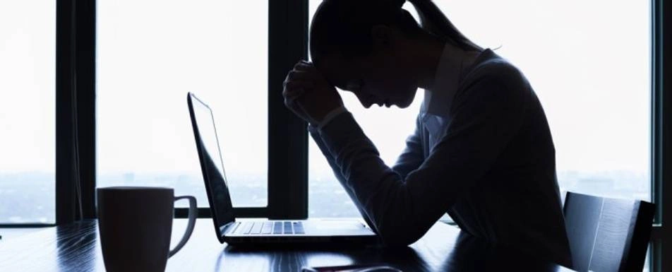 A woman crouched over a laptop resting her forehead on her fists.