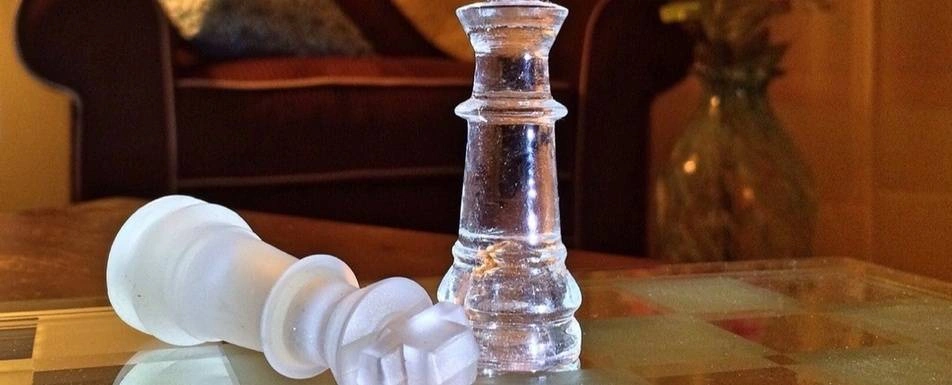 Two glass chess pieces on a glass chessboard.