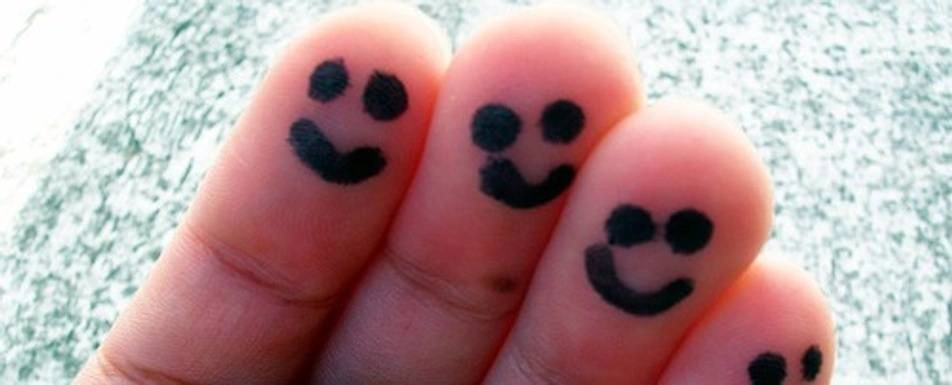 A person's fingers with smiley faces drawn on them.