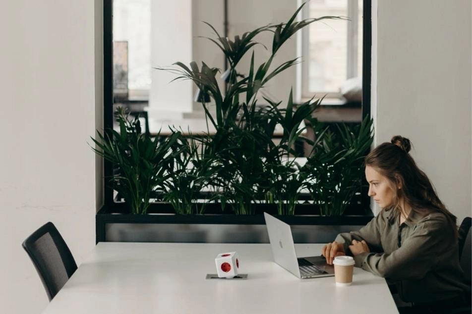 Mulher em escritório vazio, de frente a laptop, com um café.
