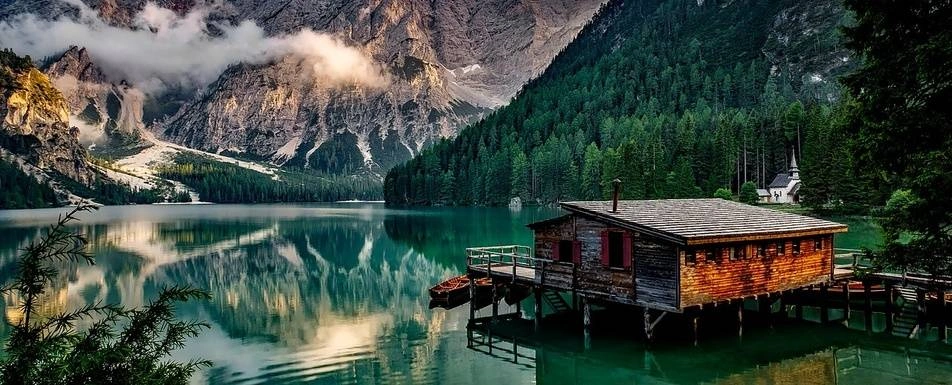 A wooden house on the water surrounded by mountains.