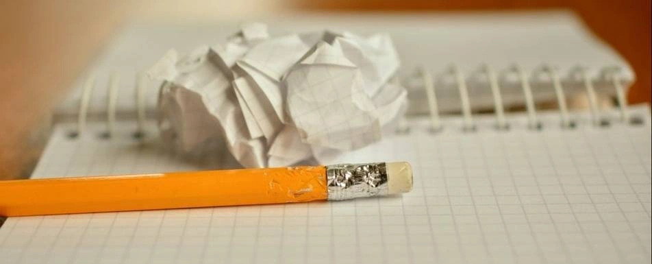 A balled up piece of paper on a notebook with a pencil next to it.