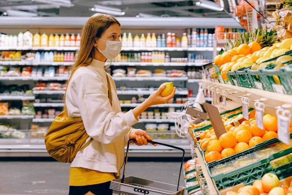 A person in a mask grocery shopping. They are holding a lemon.