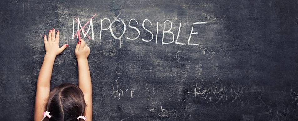 A child crossing out 'IM' in 'IMPOSSIBLE' on a chalkboard.