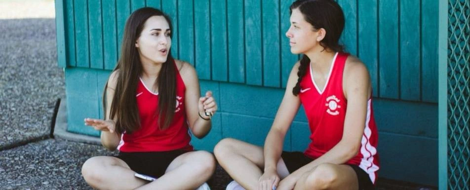 Two friends from a sport team sit chatting.