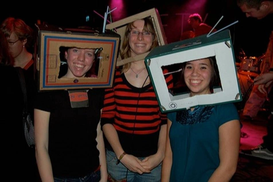 Tres chicas con una caja de cartón simulando una tele, en sus cabezas.