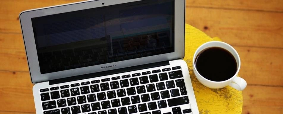 A cup of coffee next to an open macbook.
