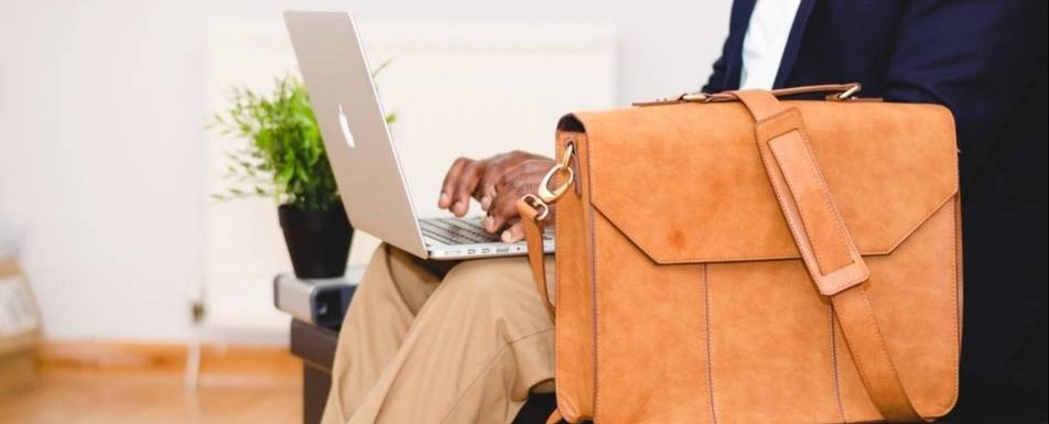 A man works at his laptop with his briefcase next to him.
