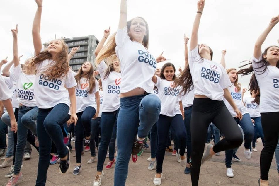 Young women in white "doing good" shirts jump in unison.