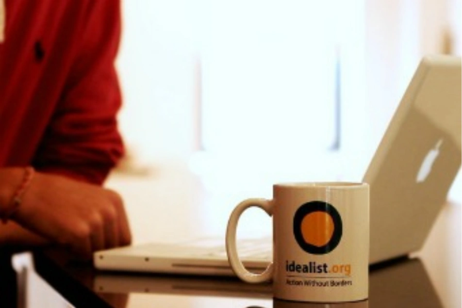 Una persona trabajando frente a un ordenador junto a una taza con el logo de Idealist.org