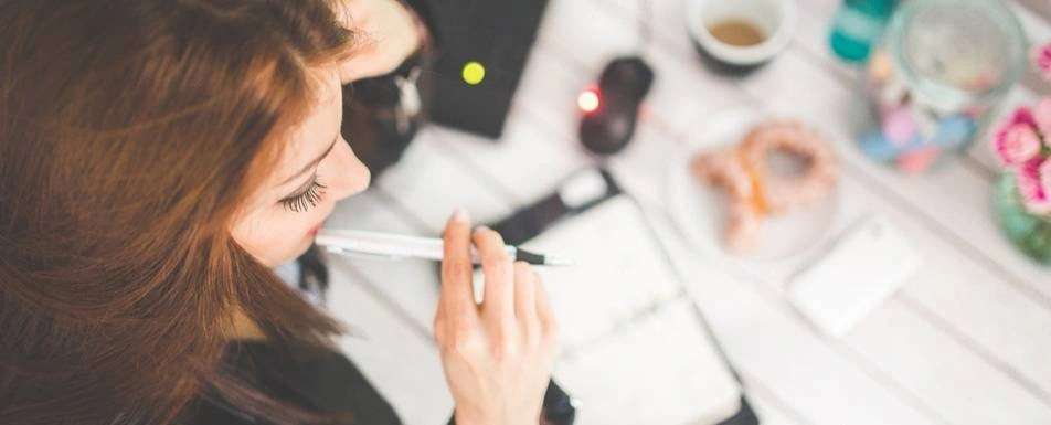 A woman thinking with a pen in her mouth.