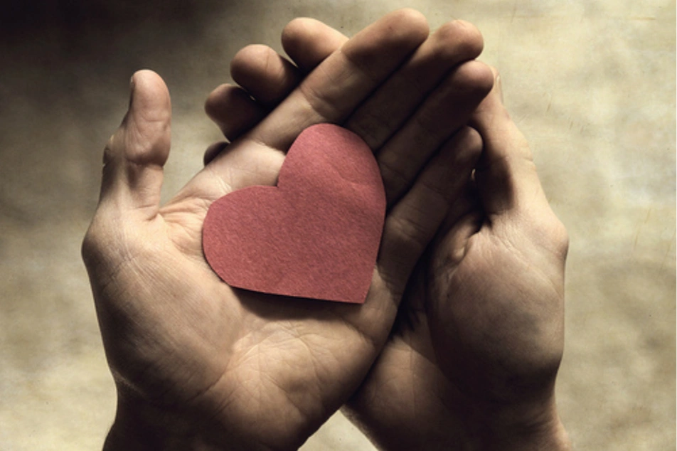 Two hands hold a paper heart.