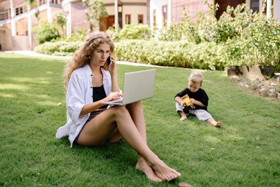 woman on laptop and phone while watching child