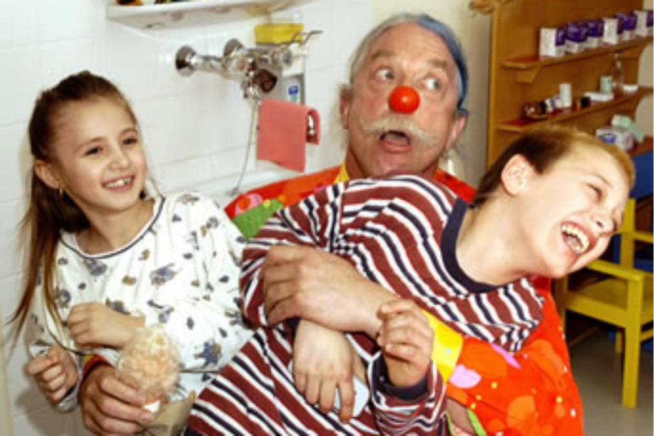Un hombre disfrazado de payaso abrazando a dos niños enfermos que mueren de risa